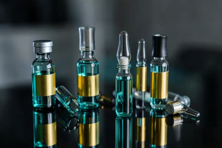 Conjunto de frascos e ampolas com rótulos dourados e brilhantes, dispostos sobre uma superfície espelhada, sugerindo luxo e eficácia.