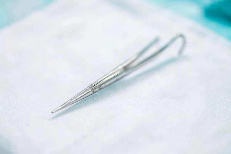 Instrumento cirúrgico fino e prateado em close-up, repousando sobre um campo cirúrgico branco e esterilizado.