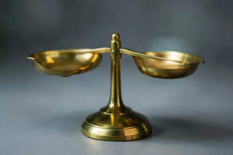 Uma balança de precisão com pratos dourados, um em cada lado, em equilíbrio perfeito sobre uma superfície neutra.